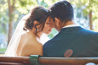 Rear view of loving couple enjoying romantic moments on their wedding day. Newlywed couple touching foreheads while leaning against each other while sitting on a park bench
