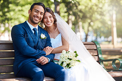 Buy stock photo Portrait of happy young couple on their wedding day. Loving bride and groom sitting together on a park bench. Newlyweds at the park for wedding photo shoot