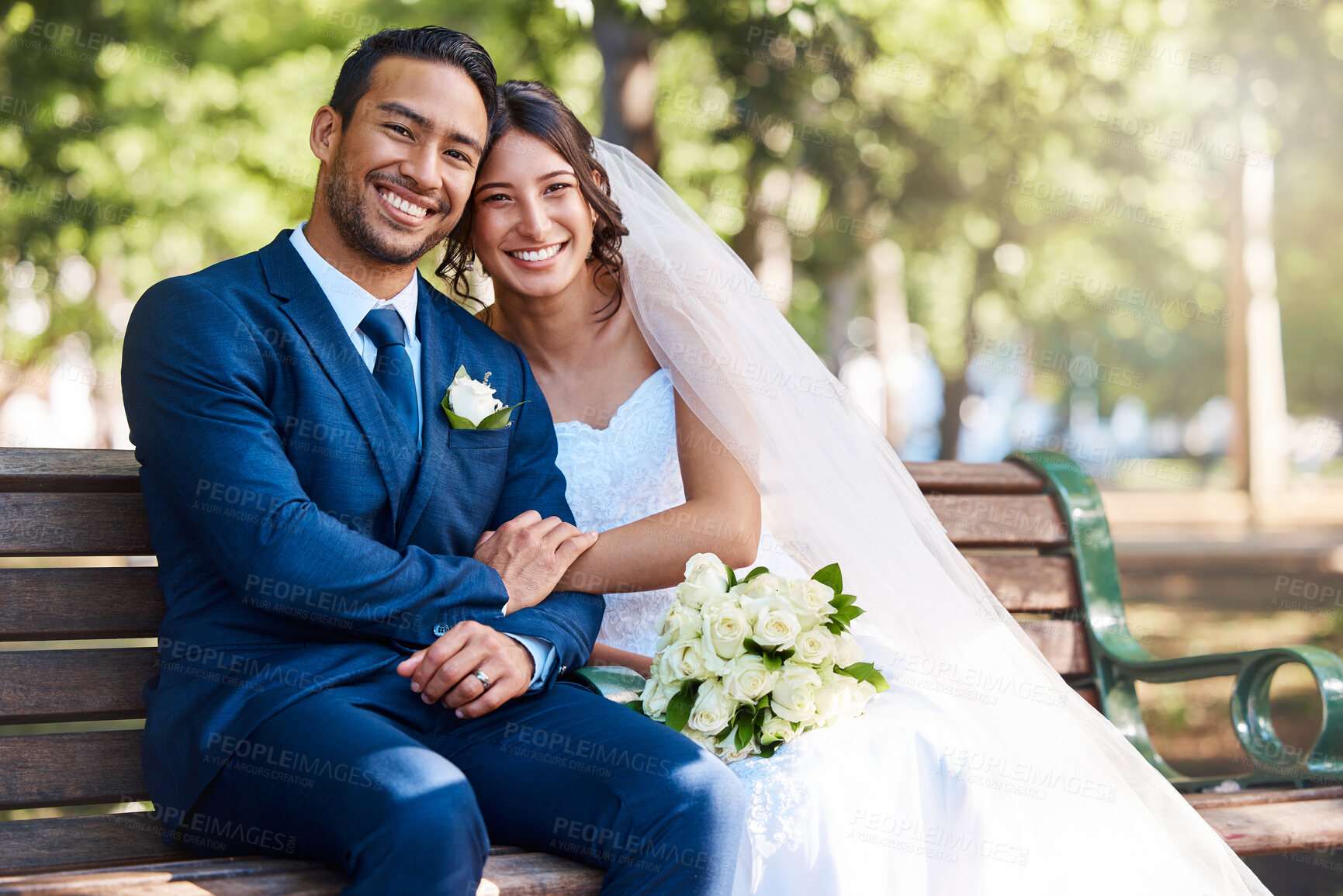 Buy stock photo Portrait of happy young couple on their wedding day. Loving bride and groom sitting together on a park bench. Newlyweds at the park for wedding photo shoot