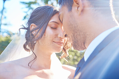 Loving young couple enjoying romantic moments on their wedding day. Newlywed couple touching foreheads on a sunny day in nature