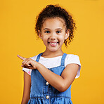 Studio portrait mixed race girl pointing sideways towards copyspace isolated against a yellow background. Cute hispanic child posing inside. Happy and cute kid showing or endorsing company or product