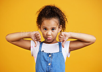Studio portrait mixed race girl giving thumbs down isolated against a yellow background. Cute hispanic child posing inside. Unhappy and upset kid being negative and saying, I disagree or disapprove