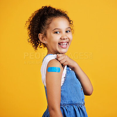 Studio portrait mixed race girl showing a plaster on her arm Isolated against a yellow background. Cute hispanic child lifting her sleeve to show injection site for covid or corona jab and vaccination