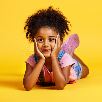 Studio portrait mixed race girl looking lying alone isolated against a yellow background. Cute hispanic child posing inside. Happy and cute kid smiling and looking carefree in casual clothes