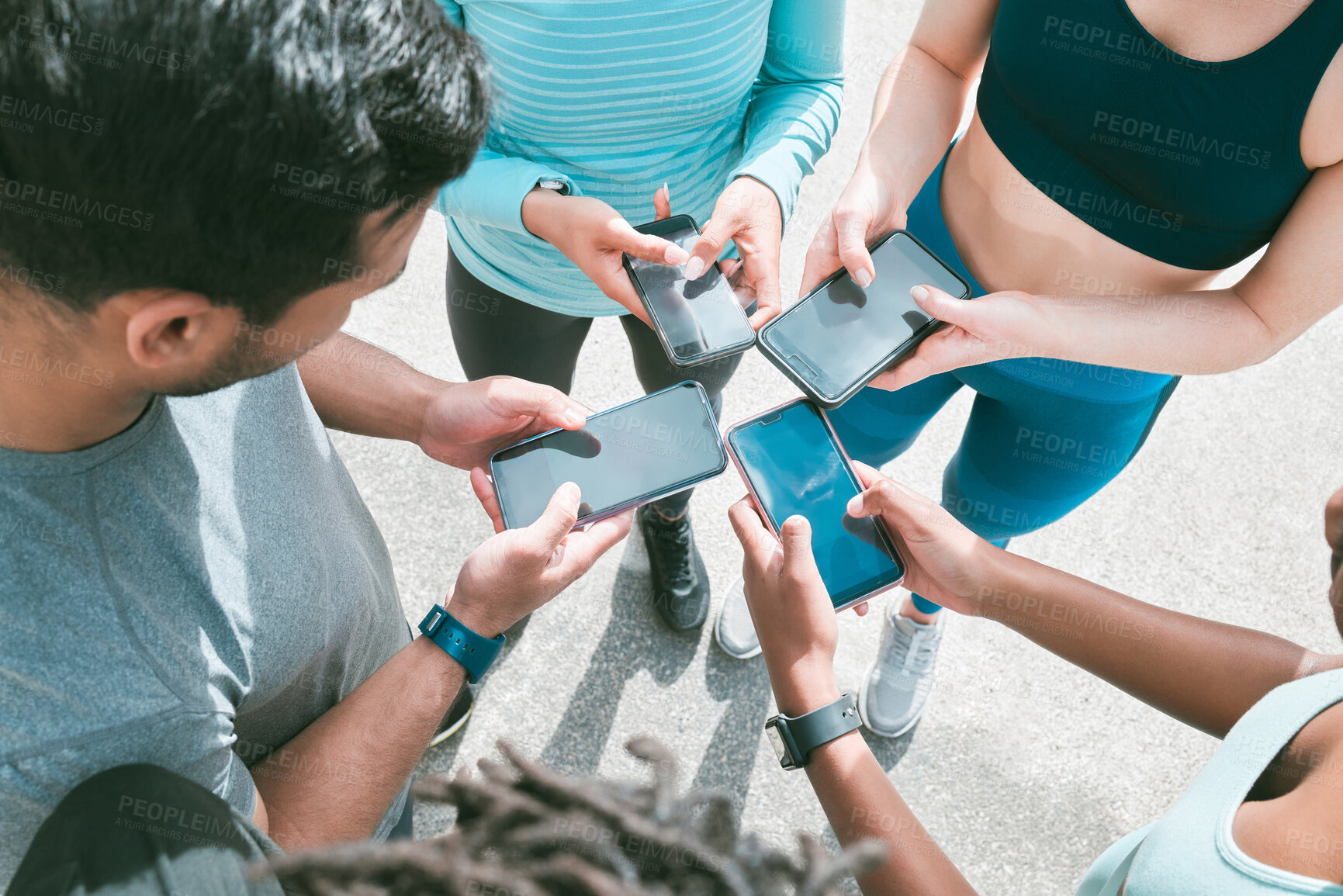 Buy stock photo Closeup of diverse group of sporty people from above using cellphones with blank screens in synchronicity while standing in a circle around each other. Hands of athletes browsing online and searching the internet in a huddle. Downloading and sharing media