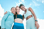 Portrait of a diverse group of happy sporty women from below standing together in a huddle for support and unity with cloudy sky in the background. Cheerful motivated athletes ready for exercise workout outside
