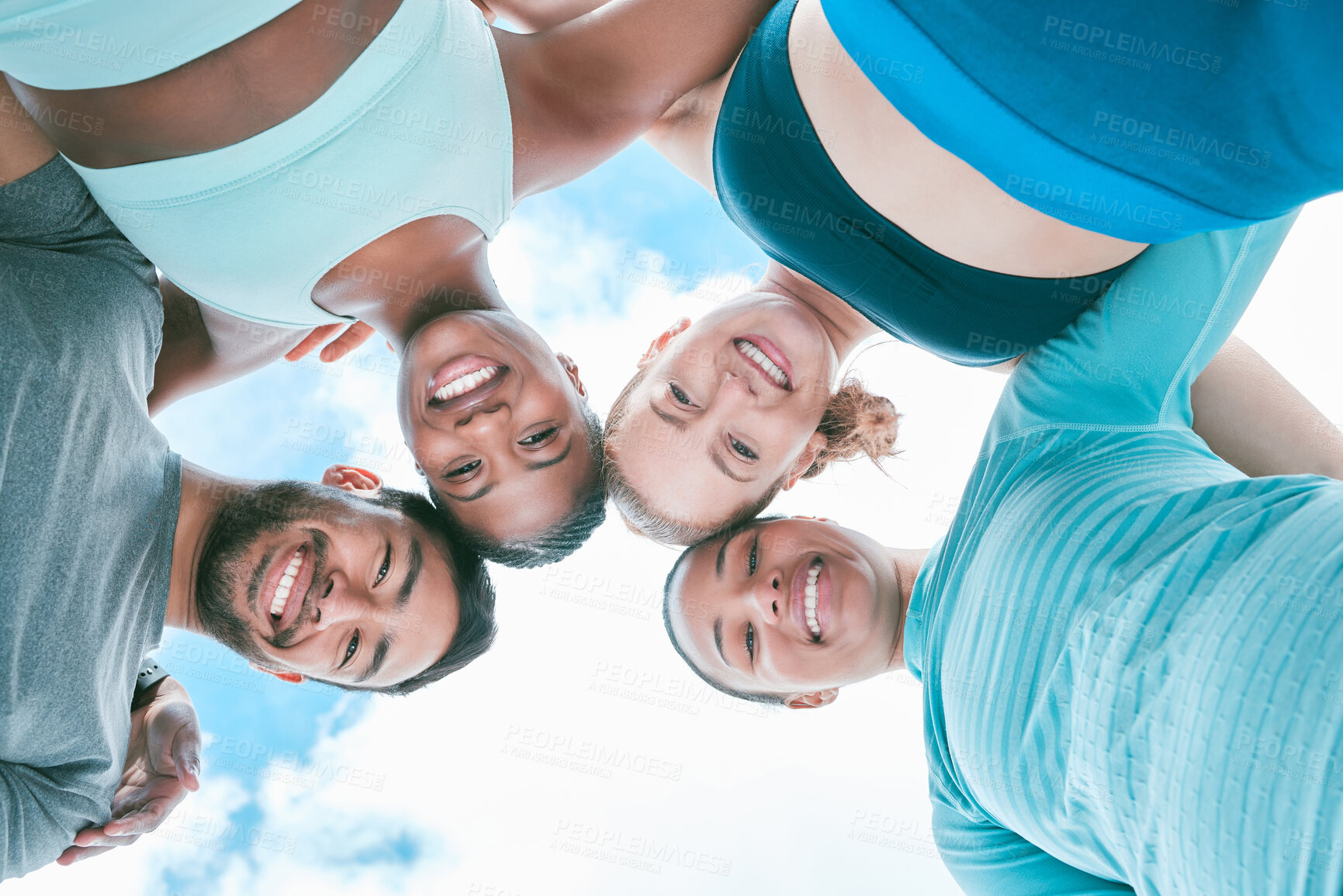 Buy stock photo Portrait of a diverse group of happy sporty people from below joining their heads together in a huddle for support and unity with cloudy sky in the background. Cheerful motivated athletes ready for exercise workout outside