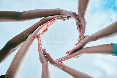 Closeup of diverse group of people from below joining hands together to form circle shape expressing unity, support and trust. Multiracial society linking for collaboration and community with cloudy sky in the background