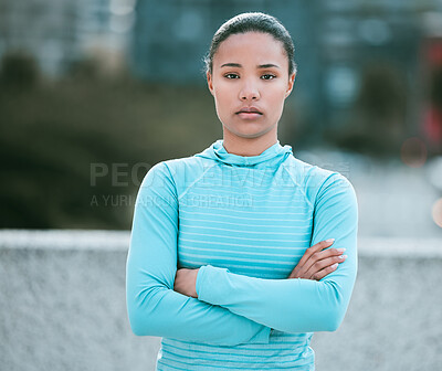 Buy stock photo Portrait of one serious young mixed race woman standing with arms crossed ready for exercise outdoors. Determined female athlete looking focused and motivated for training workout in the city
