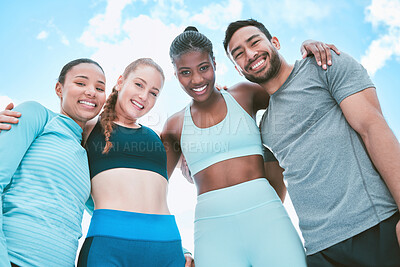 Portrait of a diverse group of happy sporty people from below standing together in a huddle for support and unity with cloudy sky in the background. Cheerful motivated athletes ready for exercise workout outside