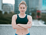 Portrait of one serious young caucasian woman standing with arms crossed ready for exercise outdoors. Determined female athlete looking focused and motivated for training workout in the city