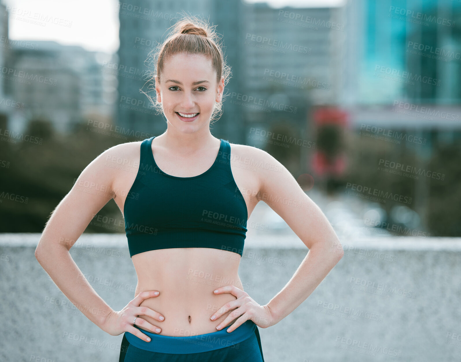 Buy stock photo Portrait of one confident young caucasian woman standing with hands on hips ready for exercise outdoors. Determined female athlete looking happy and motivated for training workout in the city