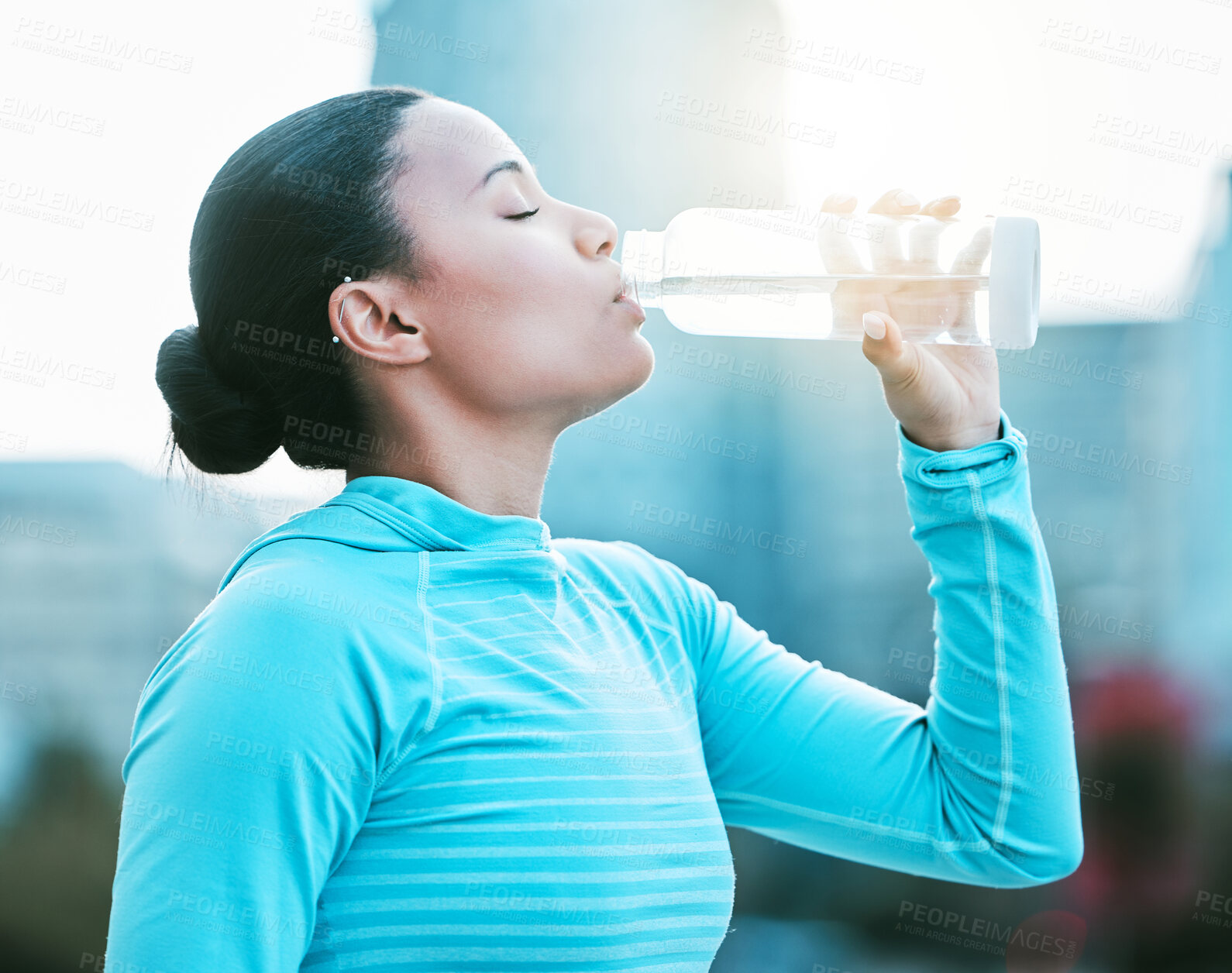 Buy stock photo One fit young mixed race woman taking a rest break to drink water from bottle while exercising outdoors. Female athlete quenching thirst and cooling down after an intense training workout in the city