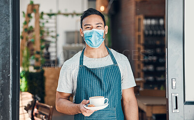 Portrait of one young hispanic waiter wearing a face mask and serving a cup of coffee while working in a cafe. Friendly barista following safety protocols during the covid pandemic while managing a coffeeshop