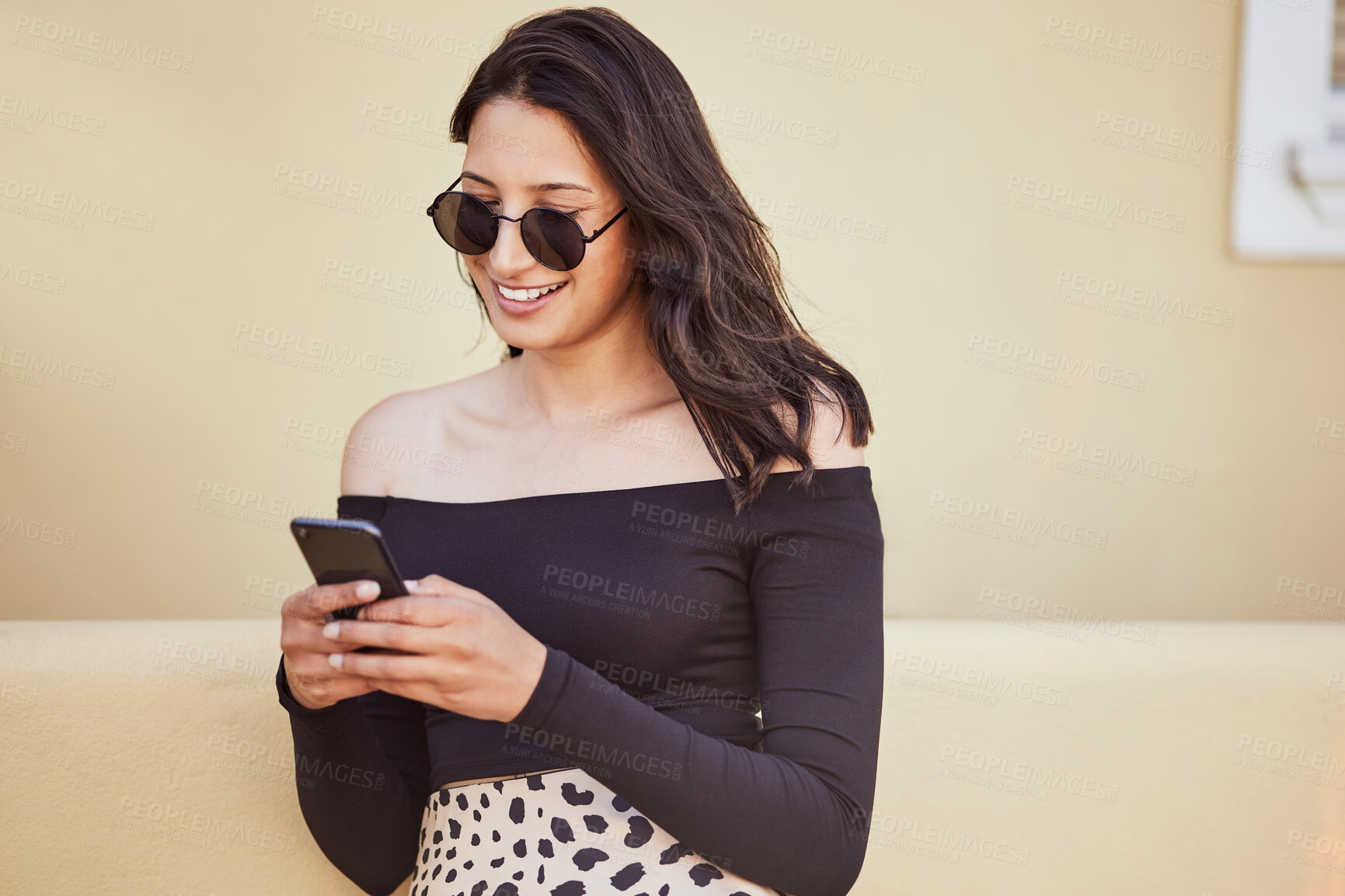 Buy stock photo Fashionable young mixed race woman with sunglasses using her smartphone while standing on sidewalk. Millennial woman sending a text or chatting on social media while on city street