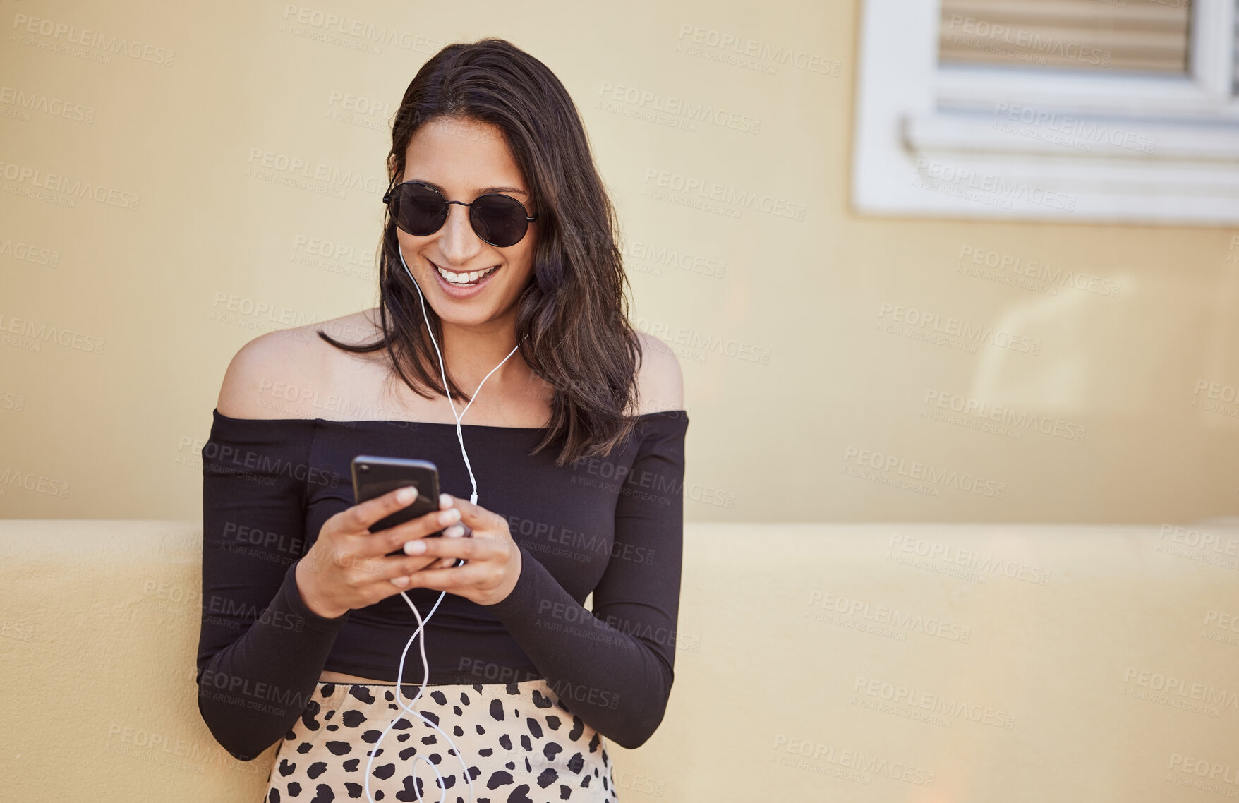 Buy stock photo Happy young woman with sunglasses using earphones to listen to music or voice note on smartphone. Pretty mixed race girl chatting while standing on sidewalk