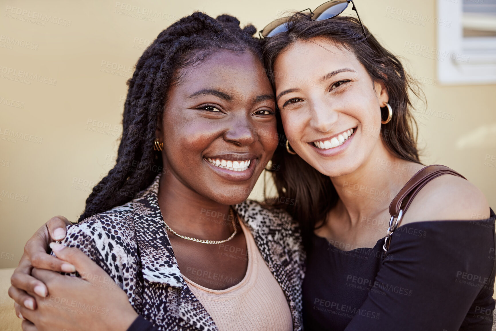 Buy stock photo Portrait of two girls hugging and smiling while standing on sidewalk, feeling joyful and happy together. Multiethnic female friends in city
