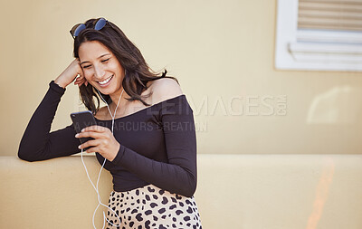 Buy stock photo Carefree young woman wearing earphones listening to music on smartphone or watching funny video. Pretty woman using mobile app while standing on sidewalk