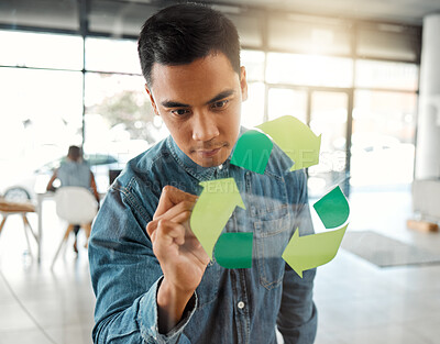 Young focused mixed race businessman drawing a recycle symbol on a glass window in an office at work. One serious hispanic businessperson designing a sign for awareness to recycling