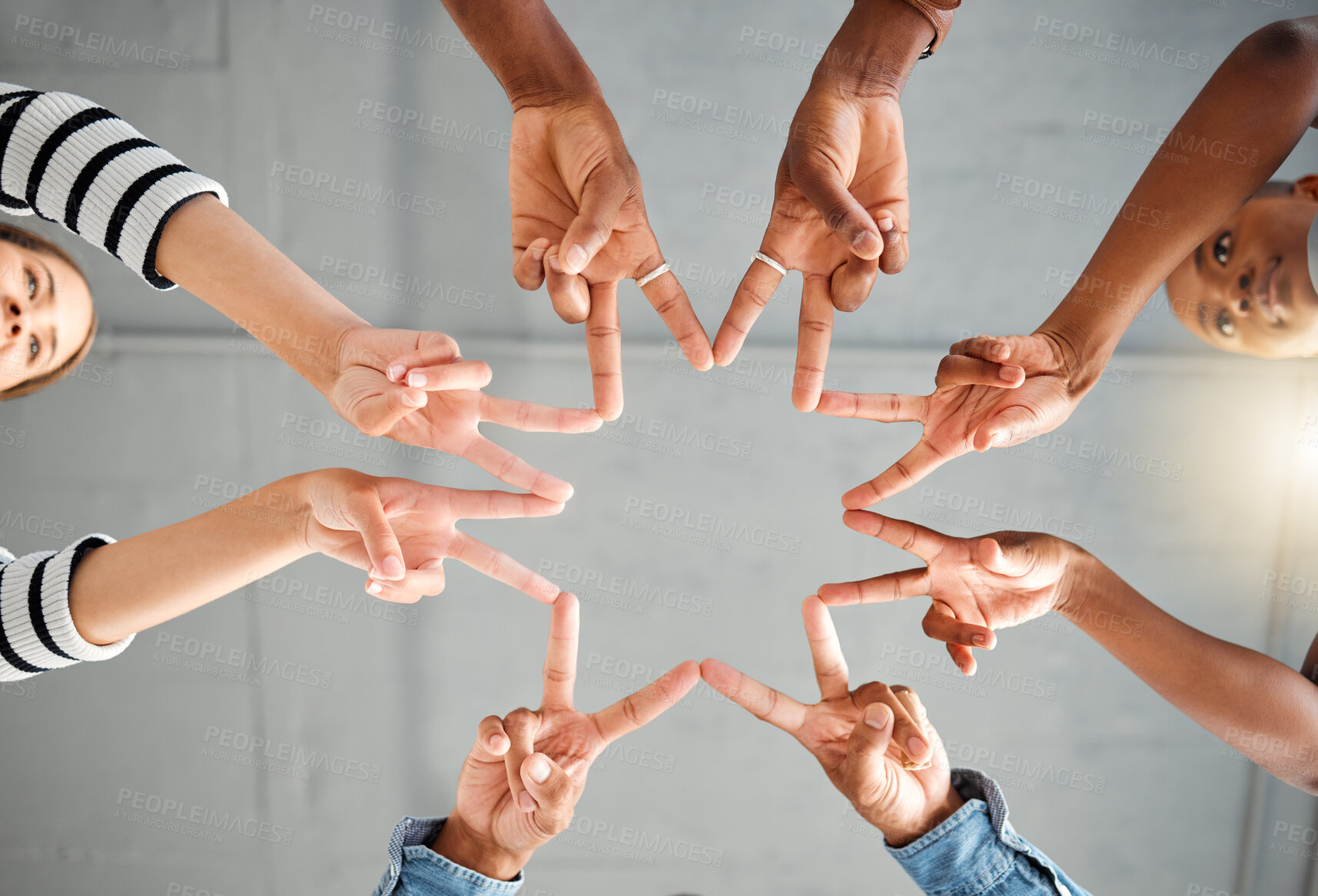 Buy stock photo Group of businesspeople making a star shape with their hands together in an office at work. Business professionals having fun making a hand gesture. Colleagues showing a peace sign from below