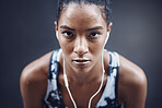 Portrait of one active young mixed race woman with sweat on her face wearing earphones and taking a rest break after run or jog exercise outdoors. Focused female athlete looking tired but determined after challenging workout against a dark background