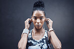 Portrait of one active young mixed race woman with sweat on her face wearing earphones and taking a rest break after run or jog exercise outdoors. Focused female athlete looking tired but determined after challenging workout against a dark background
