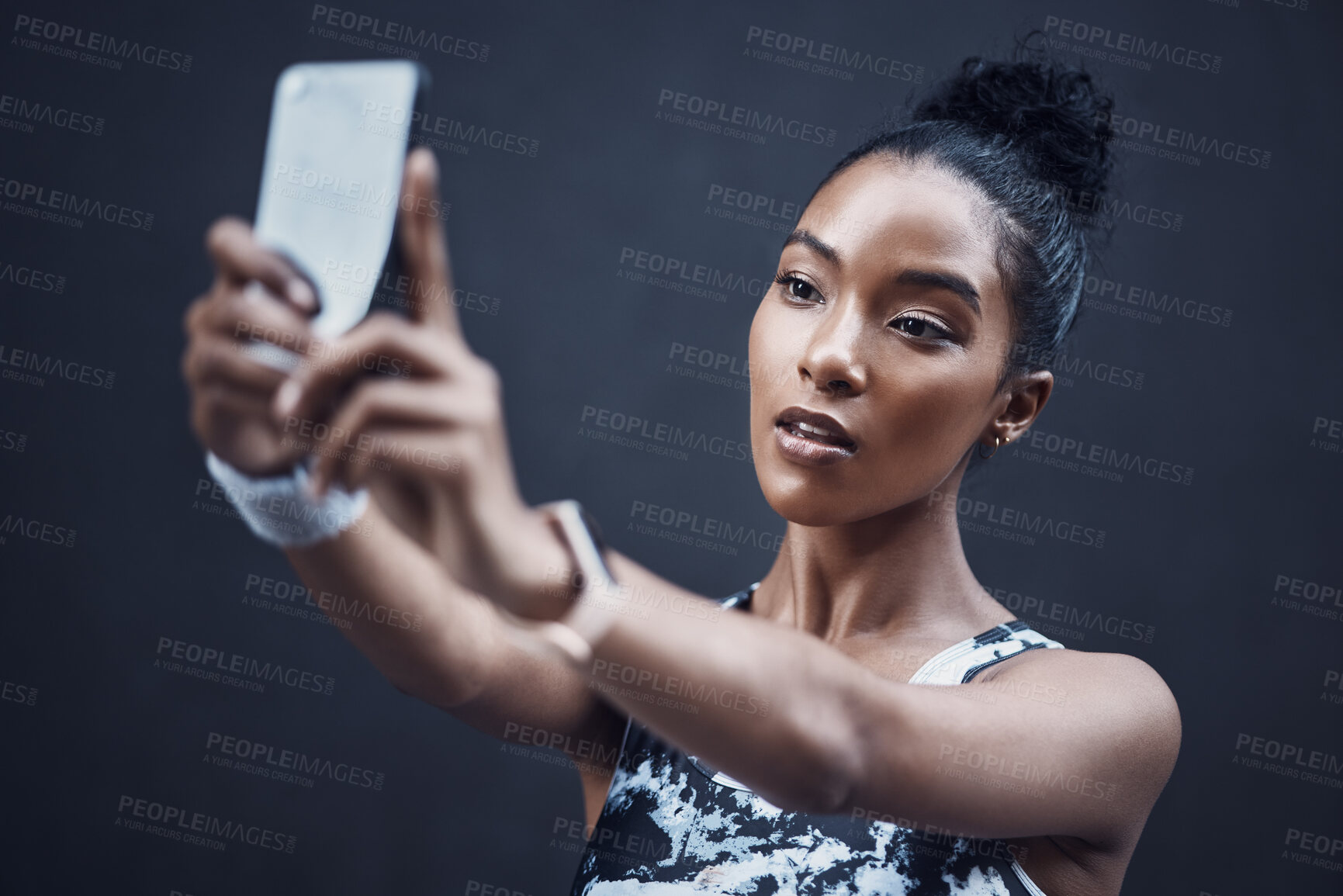 Buy stock photo One fit young mixed race woman taking selfies on a break from exercise against a dark background. Focused and determined female athlete on video call and taking photos for social media during a rest from running workout outdoors