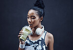 One active young mixed race woman drinking a healthy green detox smoothie while exercising outdoors. Female athlete sipping on fresh nutritious fruit juice with straw in plastic cup to cleanse, provide energy and vitamins for training