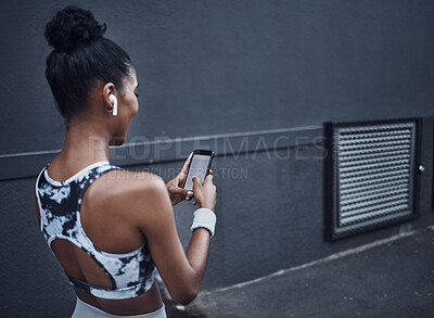 Buy stock photo Closeup of one young mixed race woman listening to music with wireless earphones from cellphone with blank screen while on break from exercise outdoors against a dark background. Female athlete texting, using fitness apps online and browsing social media