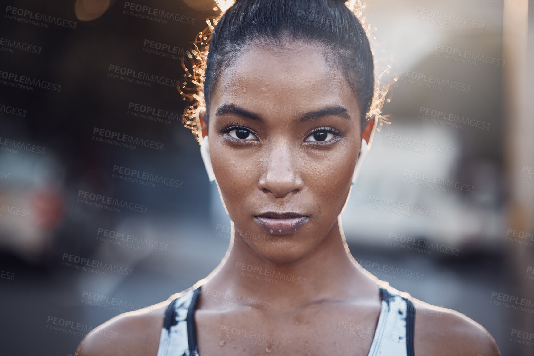 Buy stock photo Closeup portrait of one focused mixed race woman sweating after an intense workout or run in the city. Face of determined and motivated female athlete wearing earphones and taking a break from exercise outdoors