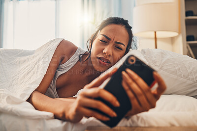 Buy stock photo A young mixed race woman looking annoyed while scrolling social media and lying in bed. An attractive Hispanic female using her cellphone and getting bad news while resting in her bedroom
