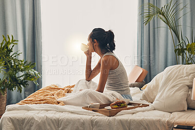 A beautiful young Hispanic woman enjoying a warm cup of coffee for breakfast. One mixed race female drinking tea while sitting in bed and daydreaming