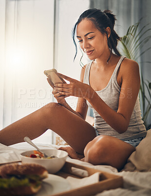 A beautiful young Hispanic woman checking social media on her cellphone while enjoying bed in breakfast at a hotel