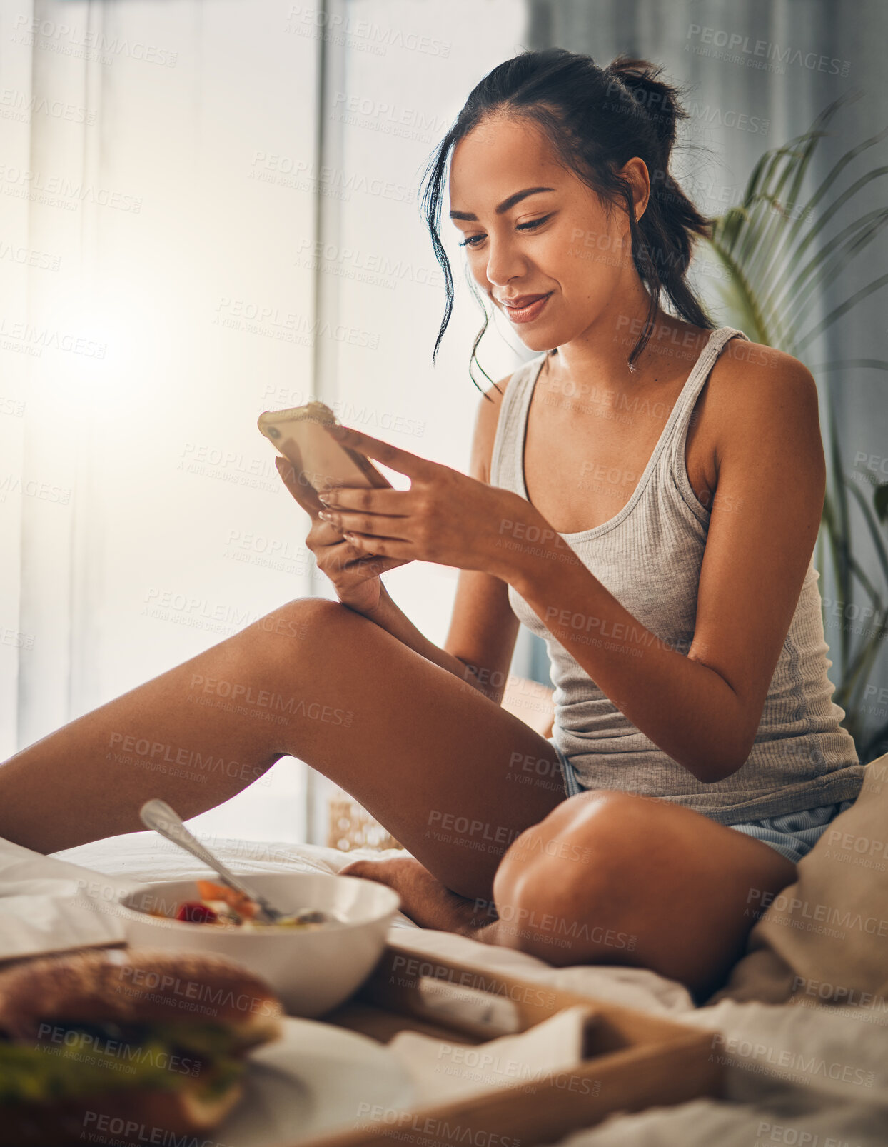Buy stock photo A beautiful young Hispanic woman checking social media on her cellphone while enjoying bed in breakfast at a hotel