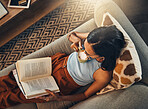 Above view of unknown mixed race woman reading book and drinking coffee in living room at home. Hispanic sitting alone on lounge sofa and enjoying novel. Feeling relaxed on weekend with fiction story