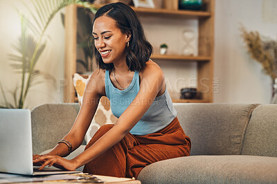 .Smiling mixed race woman browsing internet on a laptop at home. One happy hispanic entrepreneur sitting alone on her sofa and blogging over a weekend. Relaxing in a living room and typing a blog post