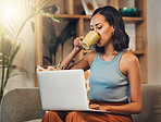Beautiful mixed race woman using laptop for blogging and drinking coffee in home living room. Hispanic entrepreneur sitting alone on lounge sofa and typing blog post on technology. Blogger remote work