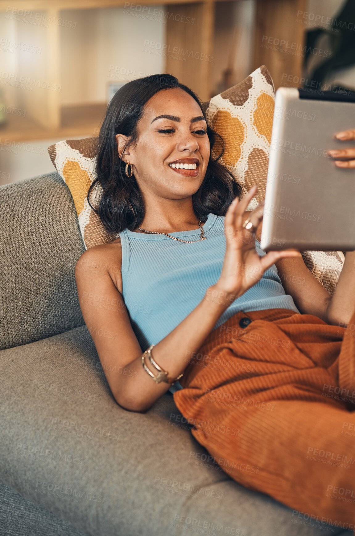 Buy stock photo Smiling mixed race woman browsing internet on digital tablet at home. Happy hispanic lying down on living room sofa alone and using technology. Relaxed woman scrolling and searching online on weekend