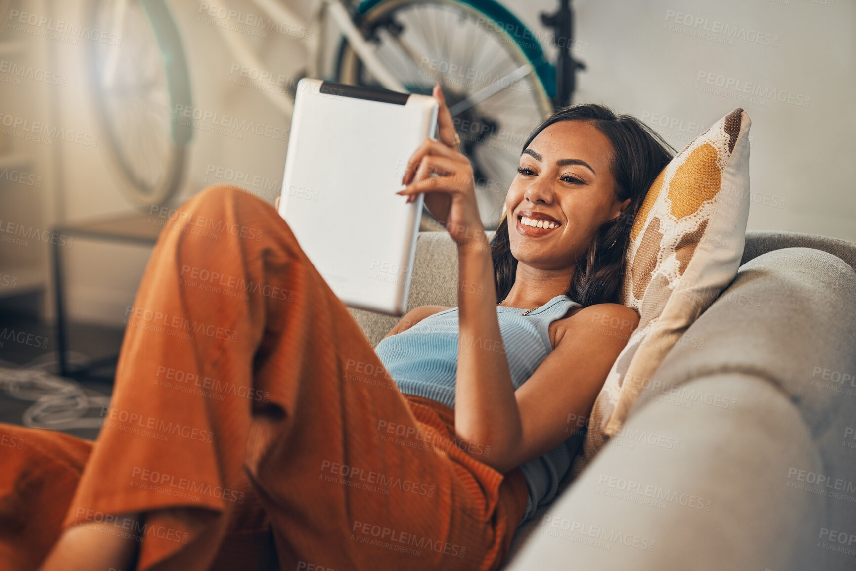 Buy stock photo Smiling mixed race woman browsing internet on digital tablet at home. Happy hispanic lying down on living room sofa alone and using technology. Relaxed woman scrolling and searching online on weekend