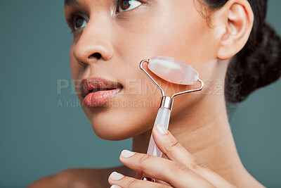 Buy stock photo Studio portrait of an attractive young woman using a face roller against a green background. Latin female using a rose roller to soften and smooth her skin