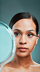 An attractive young woman using an spoolie brush and a mirror to comb her eyebrows against a green studio background. Hispanic female grooming her face by applying stylish makeup