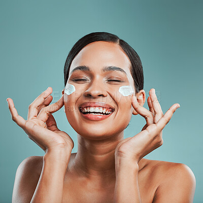 An attractive young mixed race woman posing with cream moisturiser on her face against a green studio background. Beautiful hispanic using a skin products to keep her face clean and healthy