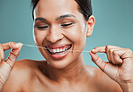 Studio portrait of an attractive young mixed race woman flossing her teeth  and smiling against a green background. Latin female taking care of her dental hygiene and oral health
