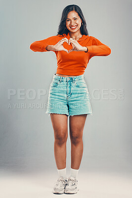 Full length portrait of mixed race woman isolated against grey studio background with copyspace. Young hispanic standing alone and making heart shape sign and symbol with hand gesture. Sharing love