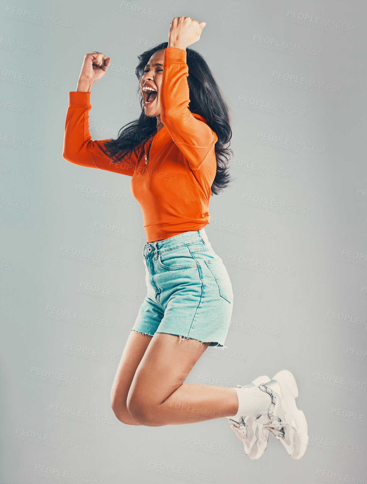 Buy stock photo Full length mixed race woman jumping and isolated against grey studio background with copyspace. Young hispanic celebrating success alone midair. Excited, cheering model making fists with hand gesture