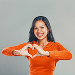 Portrait of mixed race woman isolated against grey studio background with copyspace. Young hispanic standing alone and making heart shape sign and symbol with hand gesture. Sharing love and support