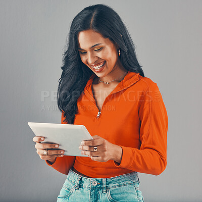 Buy stock photo Smiling mixed race woman using digital tablet while isolated against grey studio background with copyspace. Happy young hispanic standing alone while browsing the internet and networking on technology