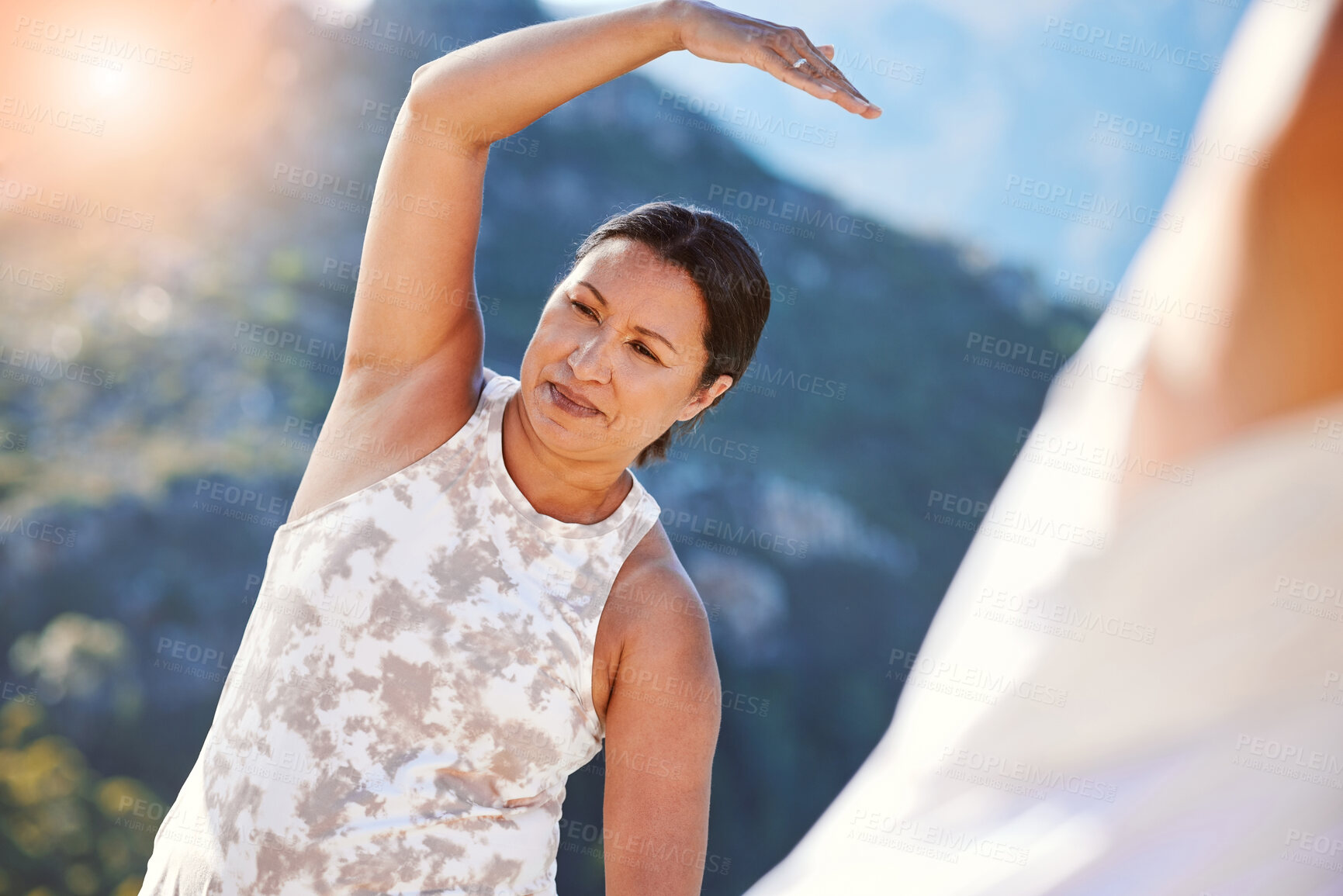 Buy stock photo Mature woman stretching her hand over her head while exercising outdoors. Mixed race woman staying fit with yoga classes. Finding inner peace, balance and living healthy