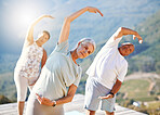 Group of senior people stretching with their hands over heads outdoors. Mature people doing yoga exercise in nature on a sunny day. Yoga class with men and women stretching together