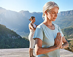 Senior woman meditating with joined hands and closed eyes breathing deeply. Class of mature people doing yoga together in nature on a sunny day